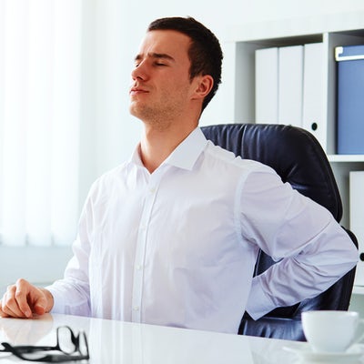 young white business man at laptop holding left arm to low back pain